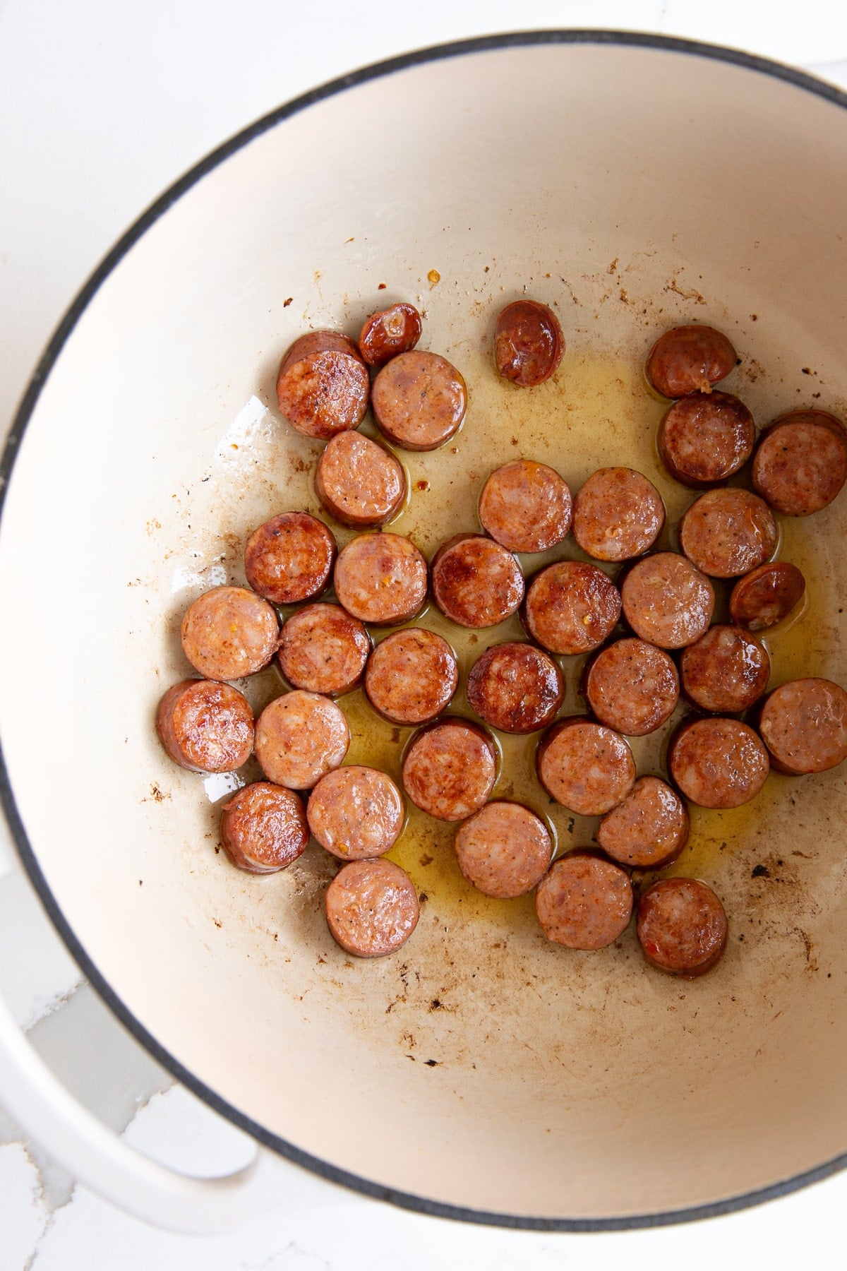 Large dutch oven filled with sliced Andouille sausage browning in oil.