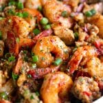 Image of a large white pot filled with cooked jambalaya made with white rice, chicken, andouille sausage, and shrimp, garnished with chopped parsley and green onions.