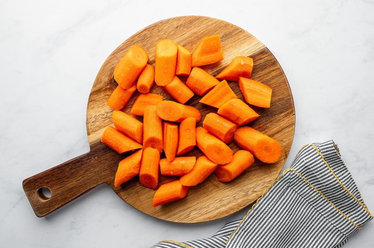 Overhead view of peeled carrots cut into large chunks on a wooden cutting board
