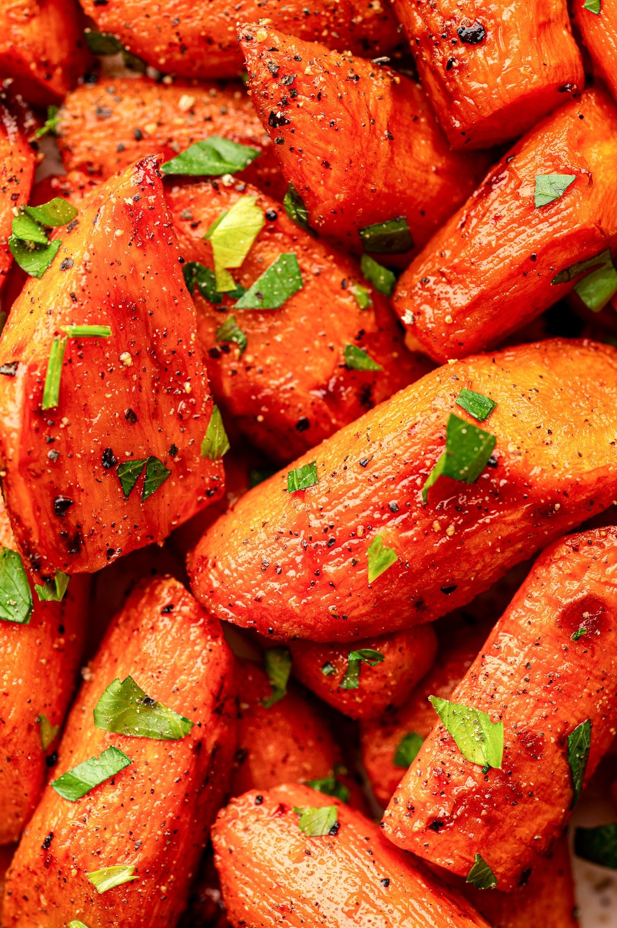 Extreme close-up of roasted carrots garnished with parsley and black pepper.
