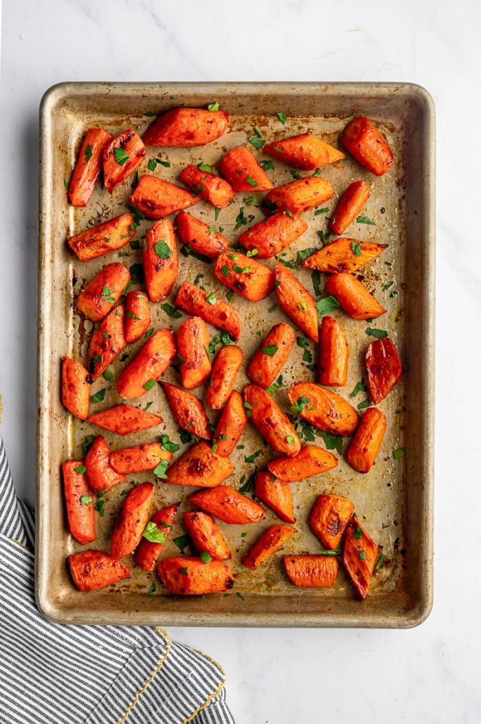 Roasted carrots with parsley scattered on a sheet pan.