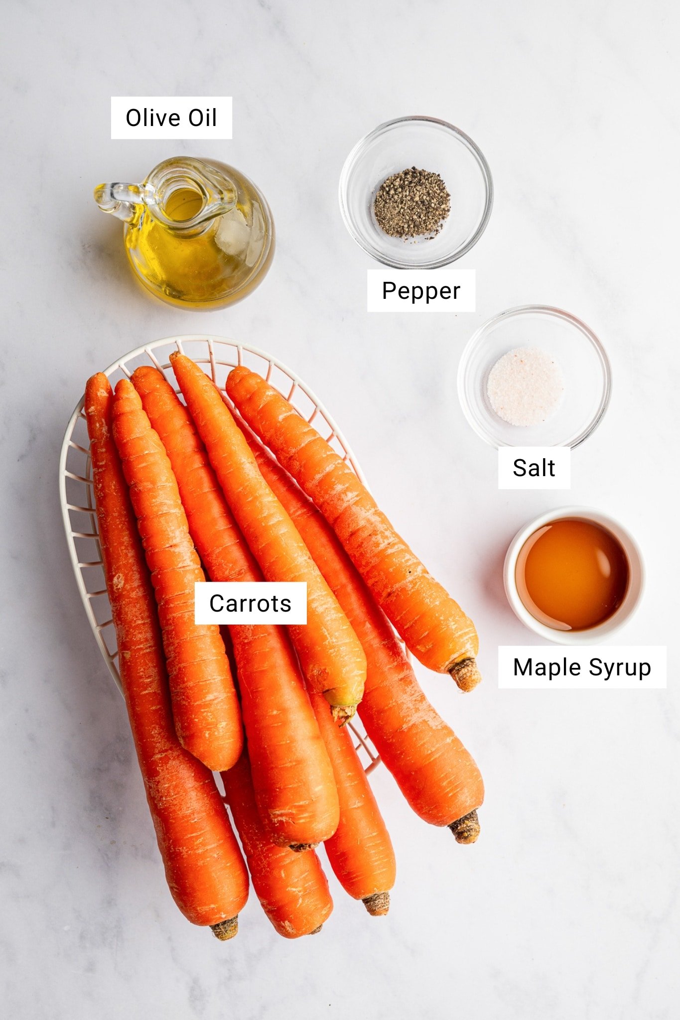 Flatlay of carrots, olive oil, salt, pepper, and maple syrup for roasted carrots.