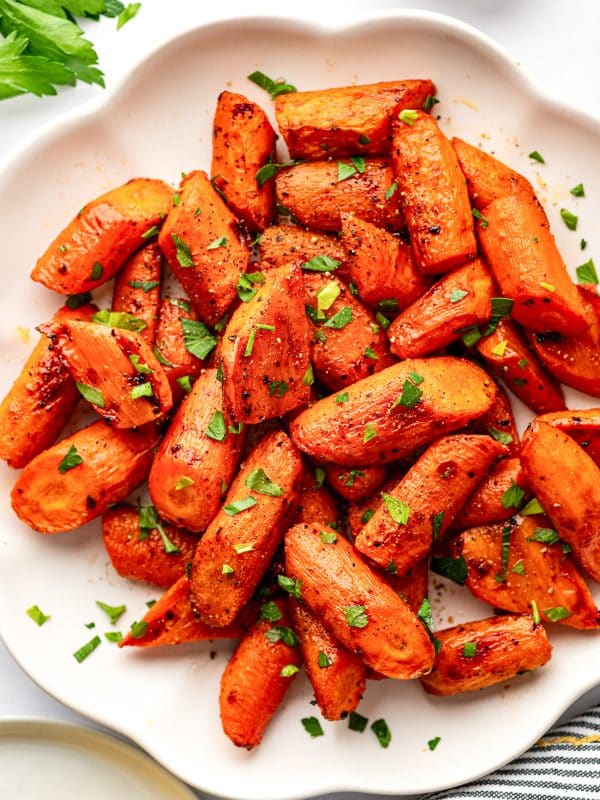 Overhead close-up of roasted carrots piled on a white serving plate.