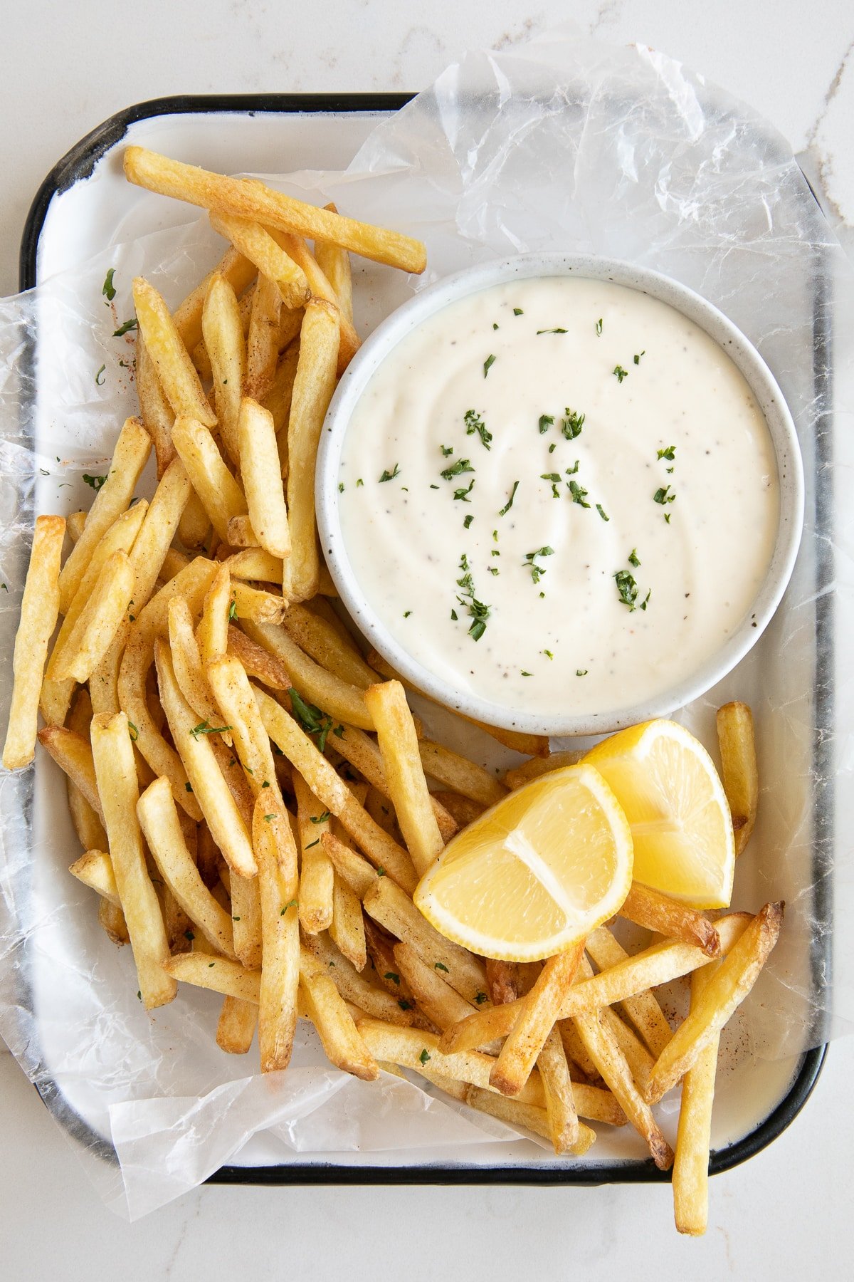 Overhead image of a small serving tray filled with fresh fries, lemon wedges, and a small shallow bowl of homemade garlic aioli.