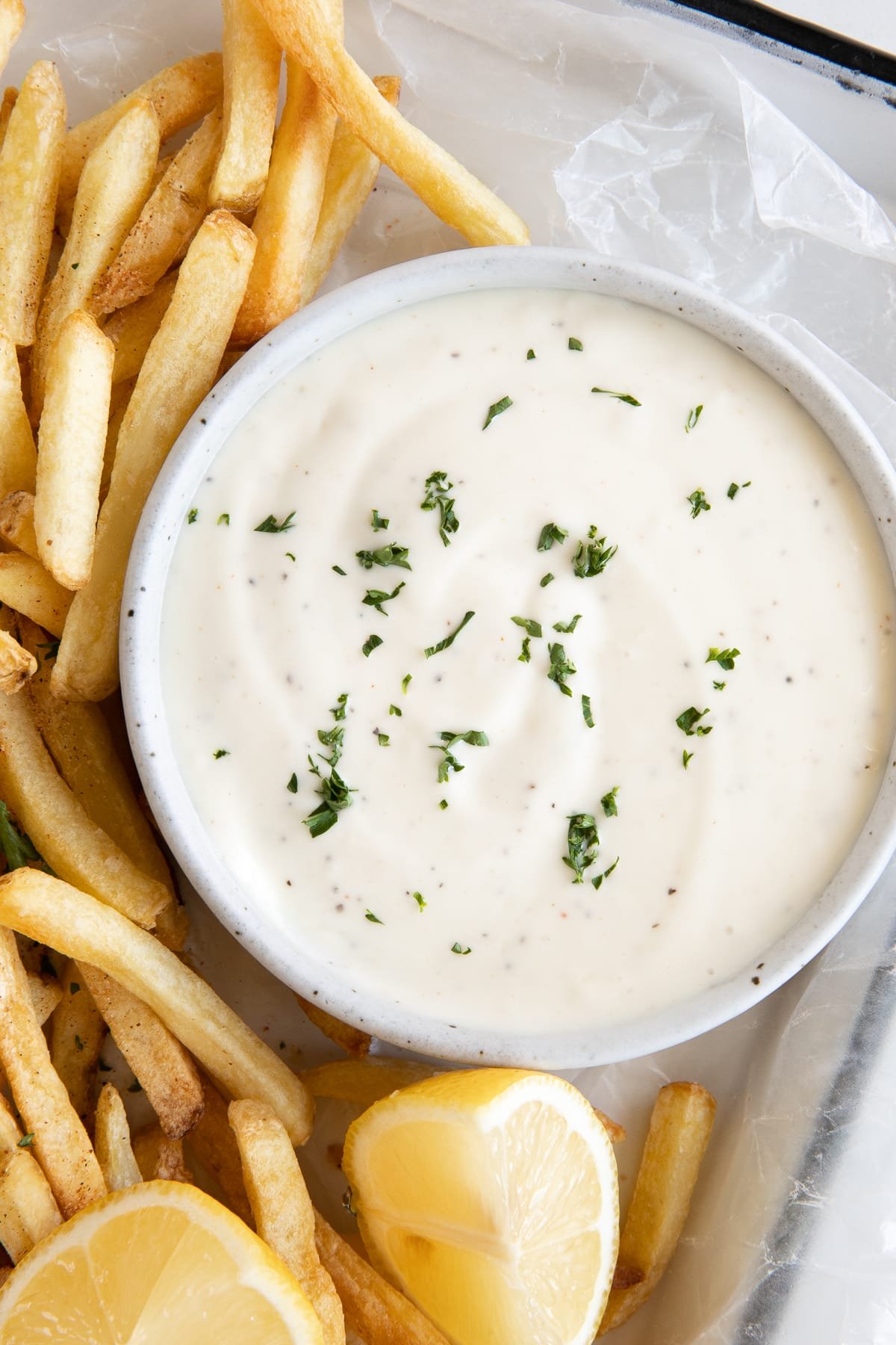 Over head image of a small round shallow bowl filled with creamy garlic aioli garnished with fresh parsley.