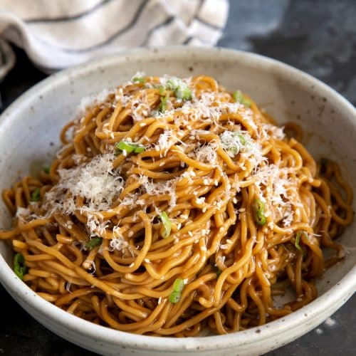 Shallow bowl filled with noodles smothered in a garlic butter and soy sauce and garnished with grated parmesan cheese and green onions.