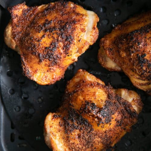 Three large cooked chicken thighs in an air fryer.