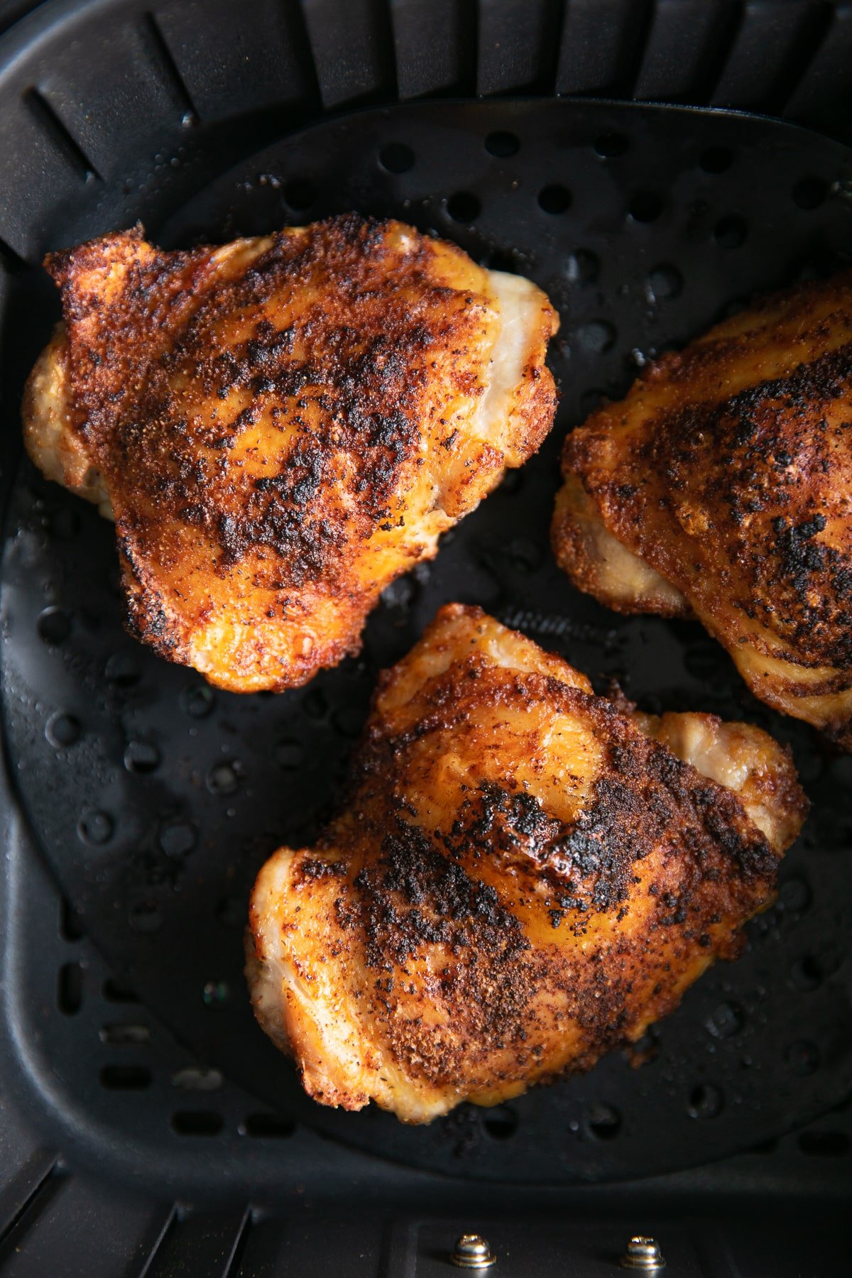 Three large cooked chicken thighs in an air fryer.
