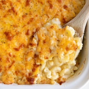 Wooden spoon filled with creamy baked macaroni and cheese in a white baking dish.