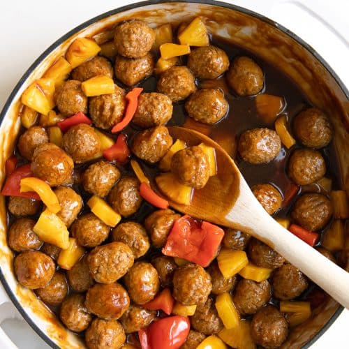 Large white skillet filled with cooked frozen meatballs, pineapple, and bell peppers in a sweet and sour sauce.