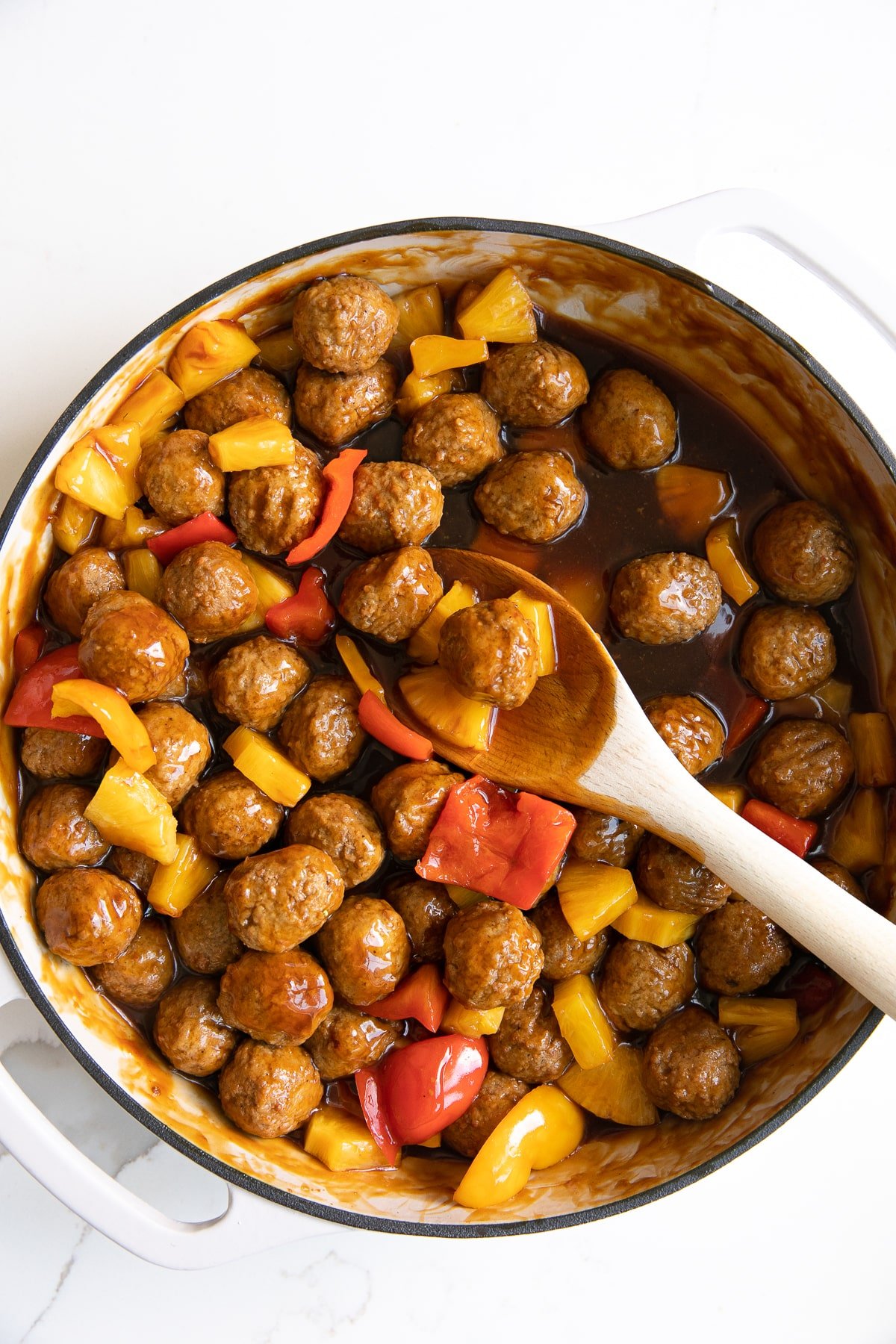 Large white skillet filled with cooked frozen meatballs, pineapple, and bell peppers in a sweet and sour sauce.