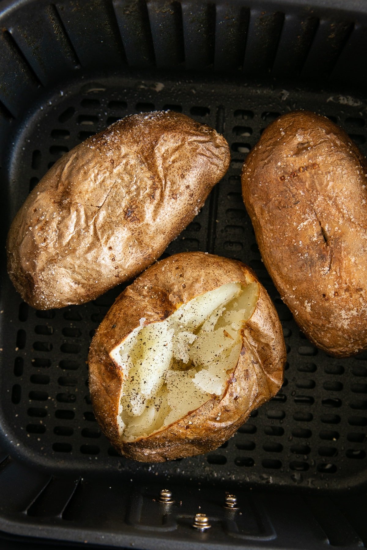Three cooked baked potatoes in an air fryer basket.