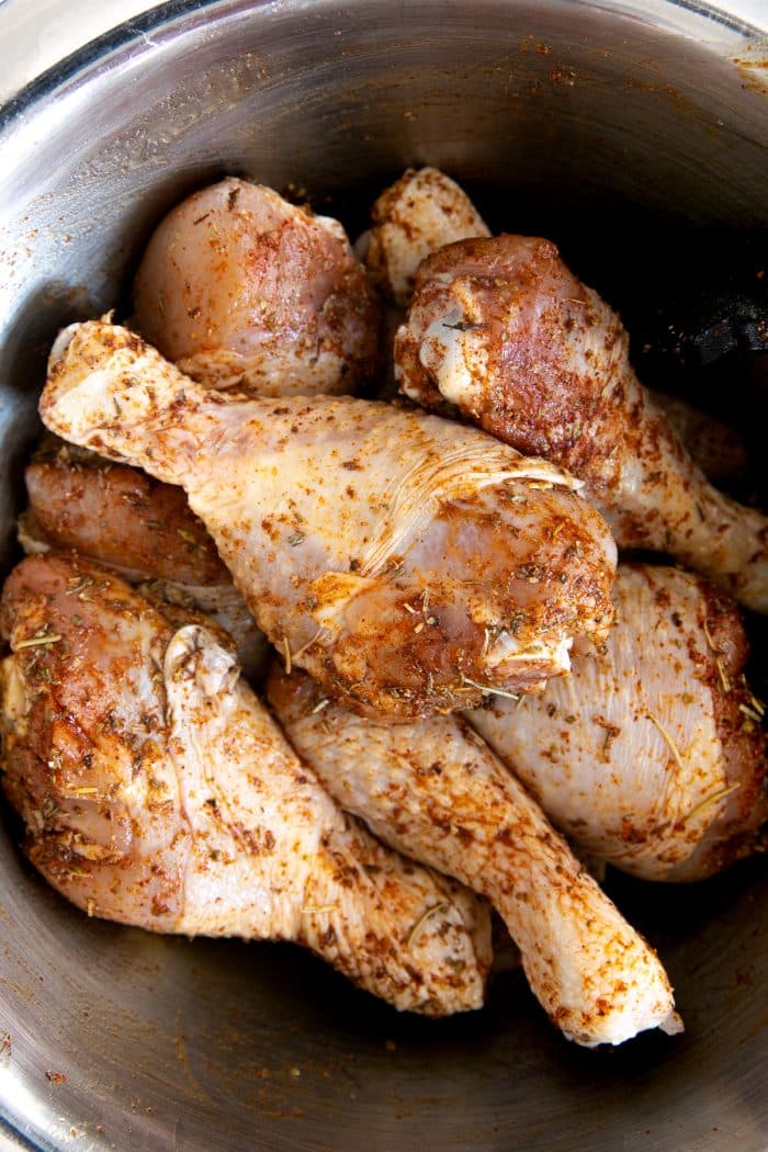 Chicken legs in a large bowl seasoned with salt, pepper, paprika, Italian seasoning, onion powder, and garlic powder.