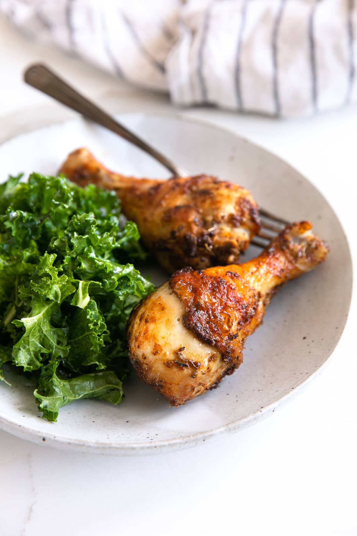 White plate with two chicken legs cooked in the air fryer and a small side of kale salad.