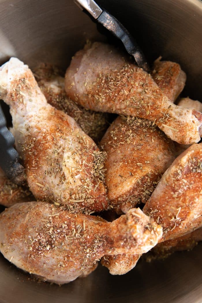 Chicken legs in a large bowl seasoned with salt, pepper, paprika, Italian seasoning, onion powder, and garlic powder.