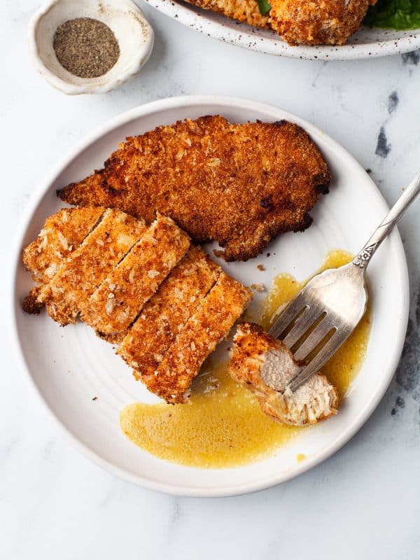 shot of sliced air fryer chicken tenders on a white plate with a pool of honey mustard sauce and a vintage fork holding a piece of chicken.