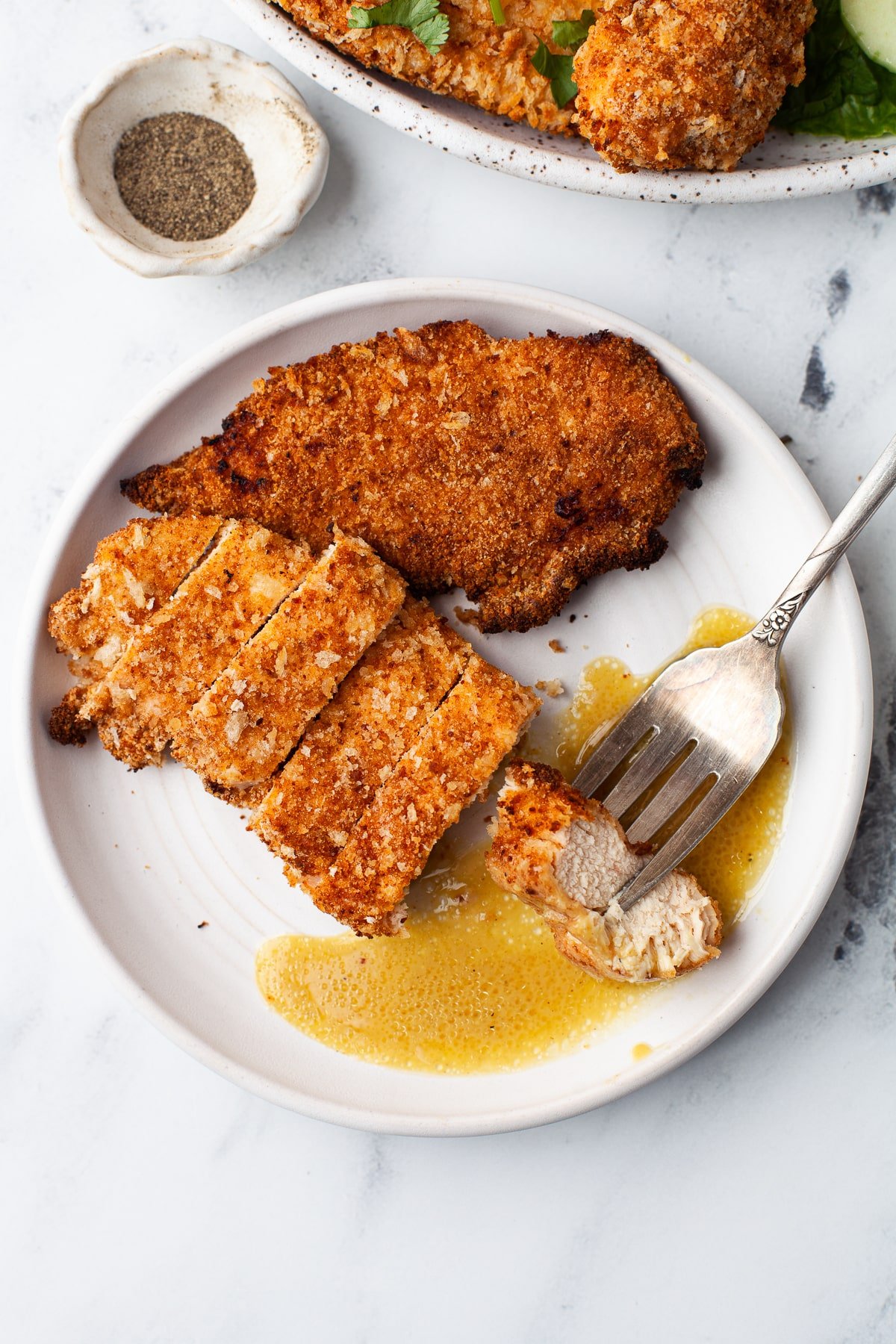 shot of sliced air fryer chicken tenders on a white plate with a pool of honey mustard sauce and a vintage fork holding a piece of chicken.