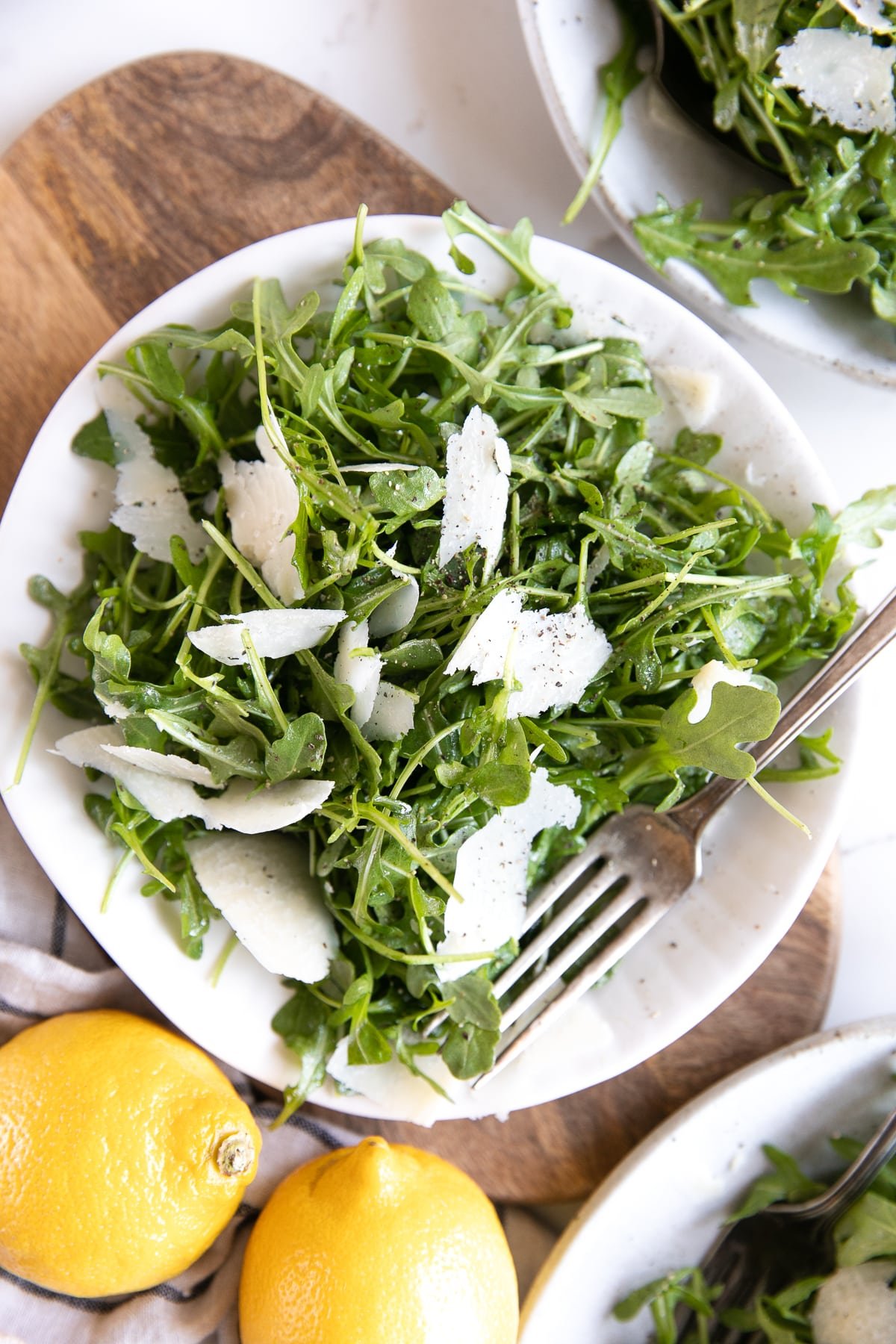 White plate with arugula and shaved parmesan salad tossed in a light lemon dressing.