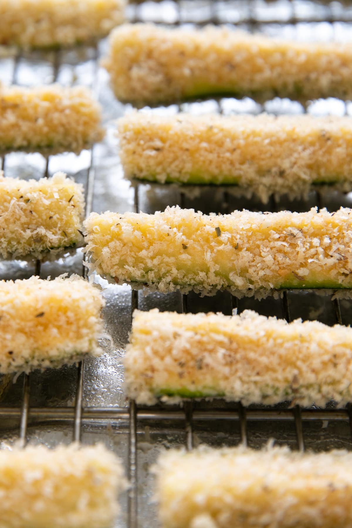 Sliced zucchini coated in panko and parmesan breadcrumbs on a wire rack before being baked.