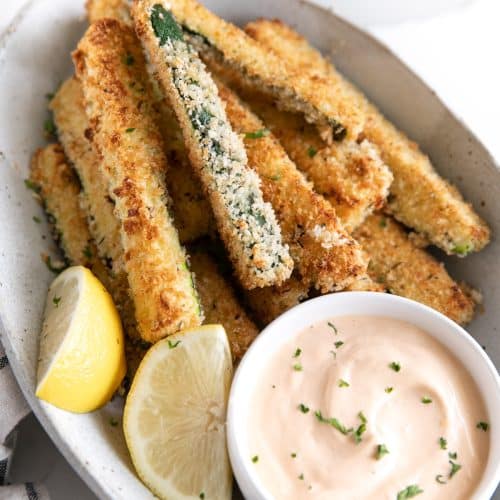 Oval serving dish with baked zucchini fries and a small bowl of chipotle mayo.