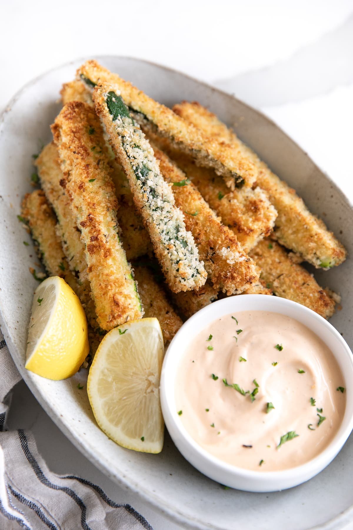 Oval serving dish with baked zucchini fries and a small bowl of chipotle mayo.