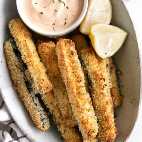 Oval serving dish with baked zucchini fries and a small bowl of chipotle mayo.