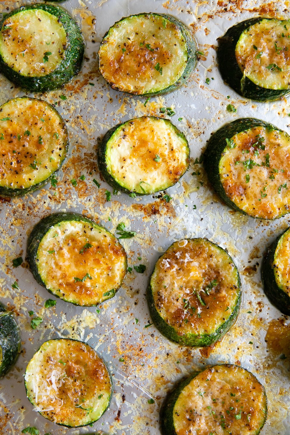 Baking sheet with roasted zucchini slices seasoned with salt, pepper, paprika, and parmesan cheese.