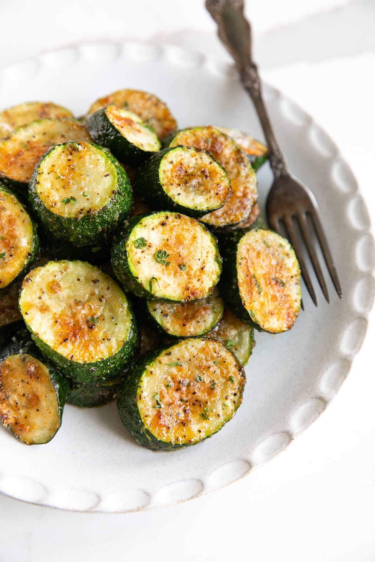 Small white plate filled with roasted zucchini with parmesan cheese.