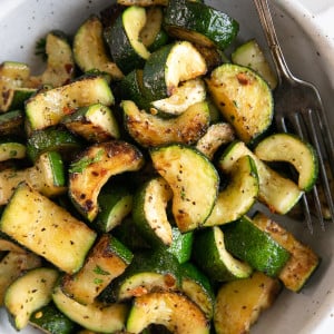 White serving bowl filled with sauteed zucchini.