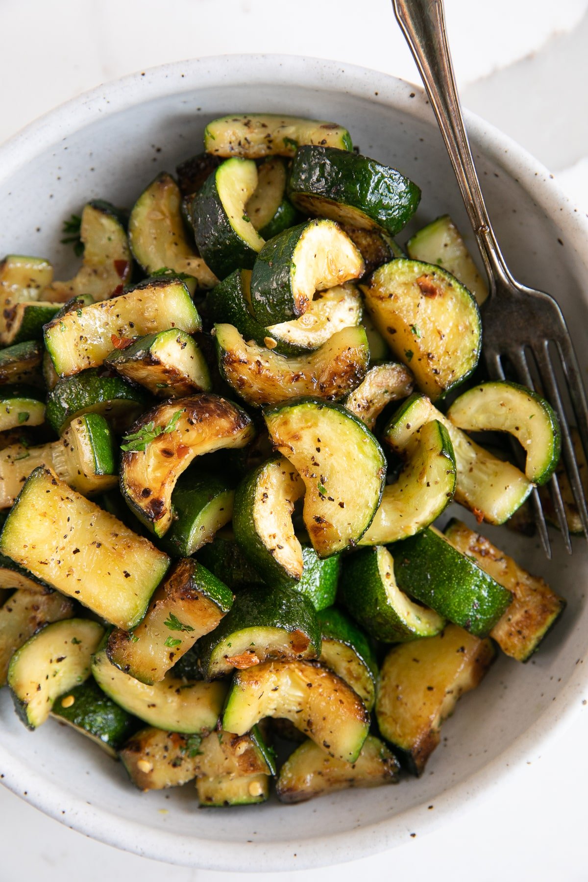 White serving bowl filled with sauteed zucchini.