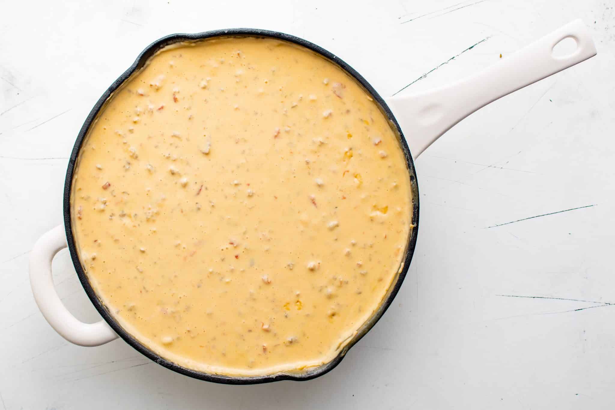 Overhead shot of a skillet filled with fully combined Sausage Cheese Dip, creamy orange with visible flecks of tomato and sausage.