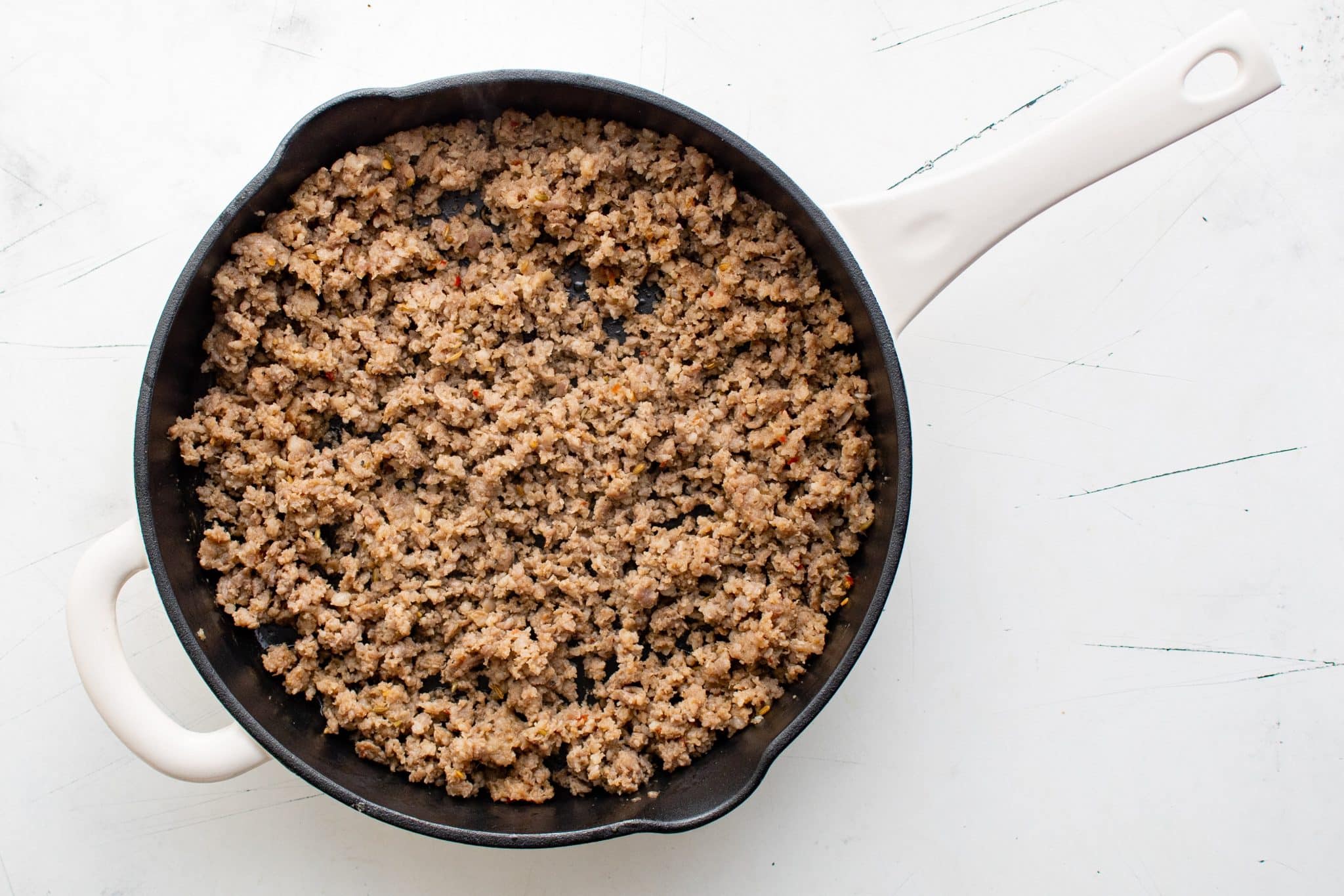 Overhead view of browned and crumbled sausage filling a skillet, fully cooked.