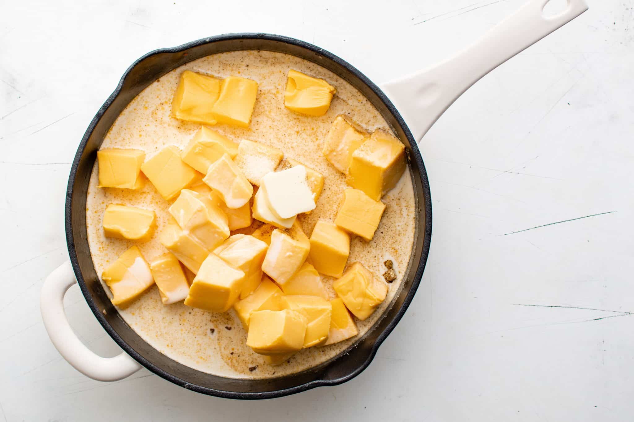 Large skillet with cubed Velveeta cheese, butter, and evaporated milk, beginning to melt into a smooth base for sausage Cheese Dip.