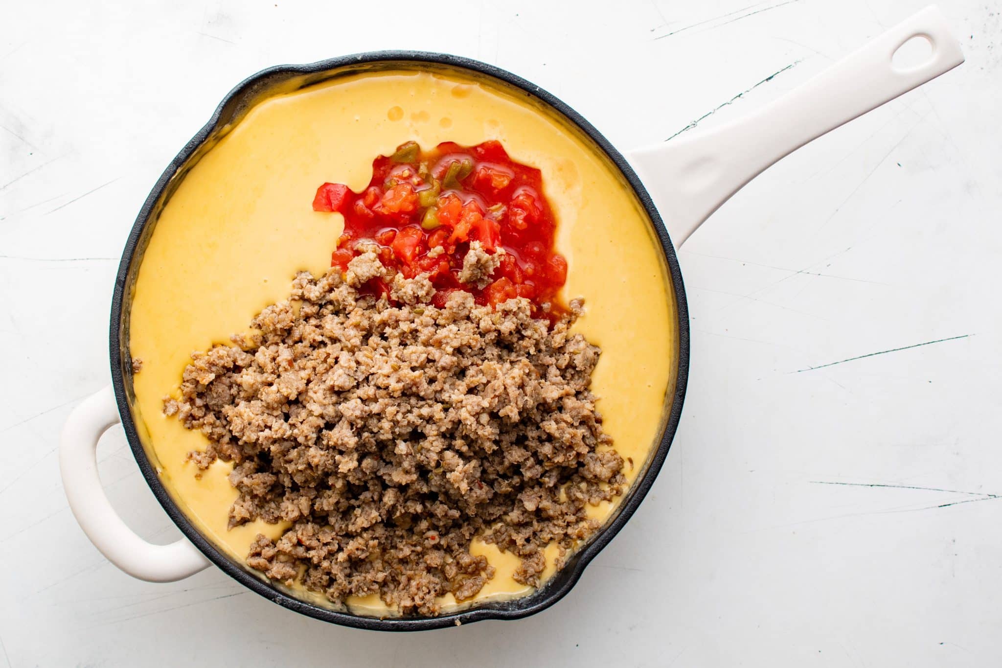 Skillet of melted Velveeta with cooked sausage crumbles and a scoop of Rotel tomatoes on top before mixing together.