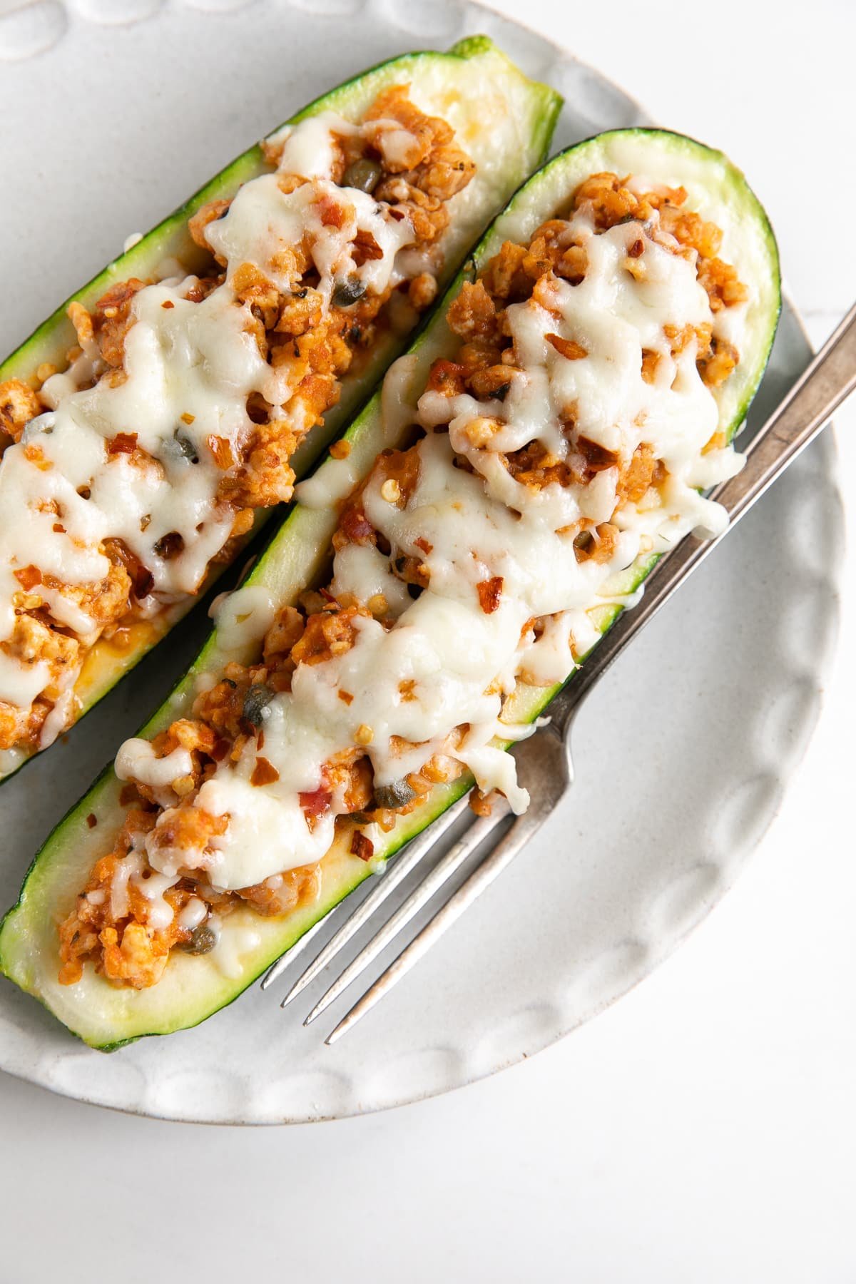 White plate with two stuffed zucchini boats filled with ground sausage and topped with melted cheese,