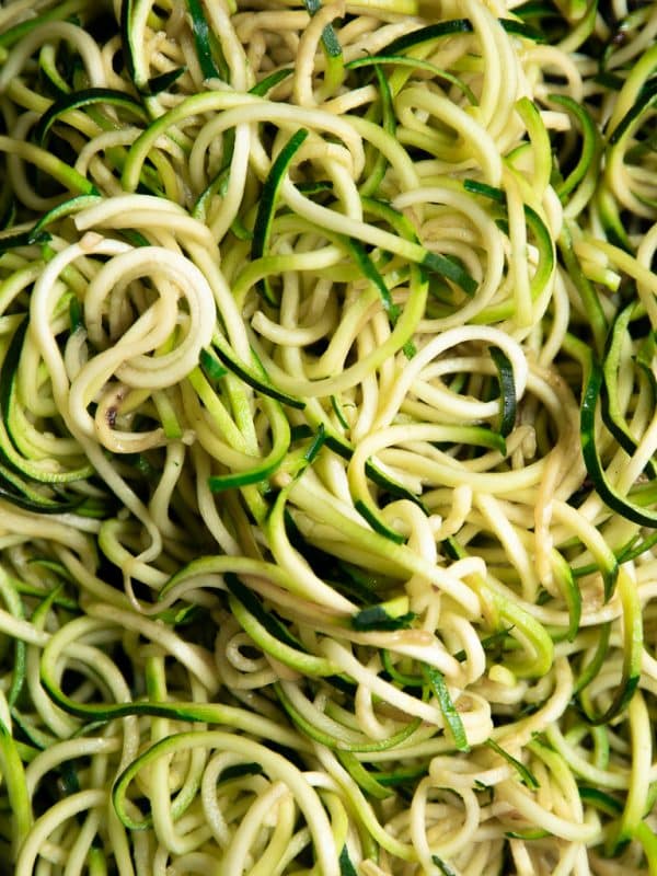 Close-up view of cooked green and pale zucchini noodles filling the entire frame, showing their long spiral shape and tender, glossy texture. No bowl, garnishes, or text overlay are visible.