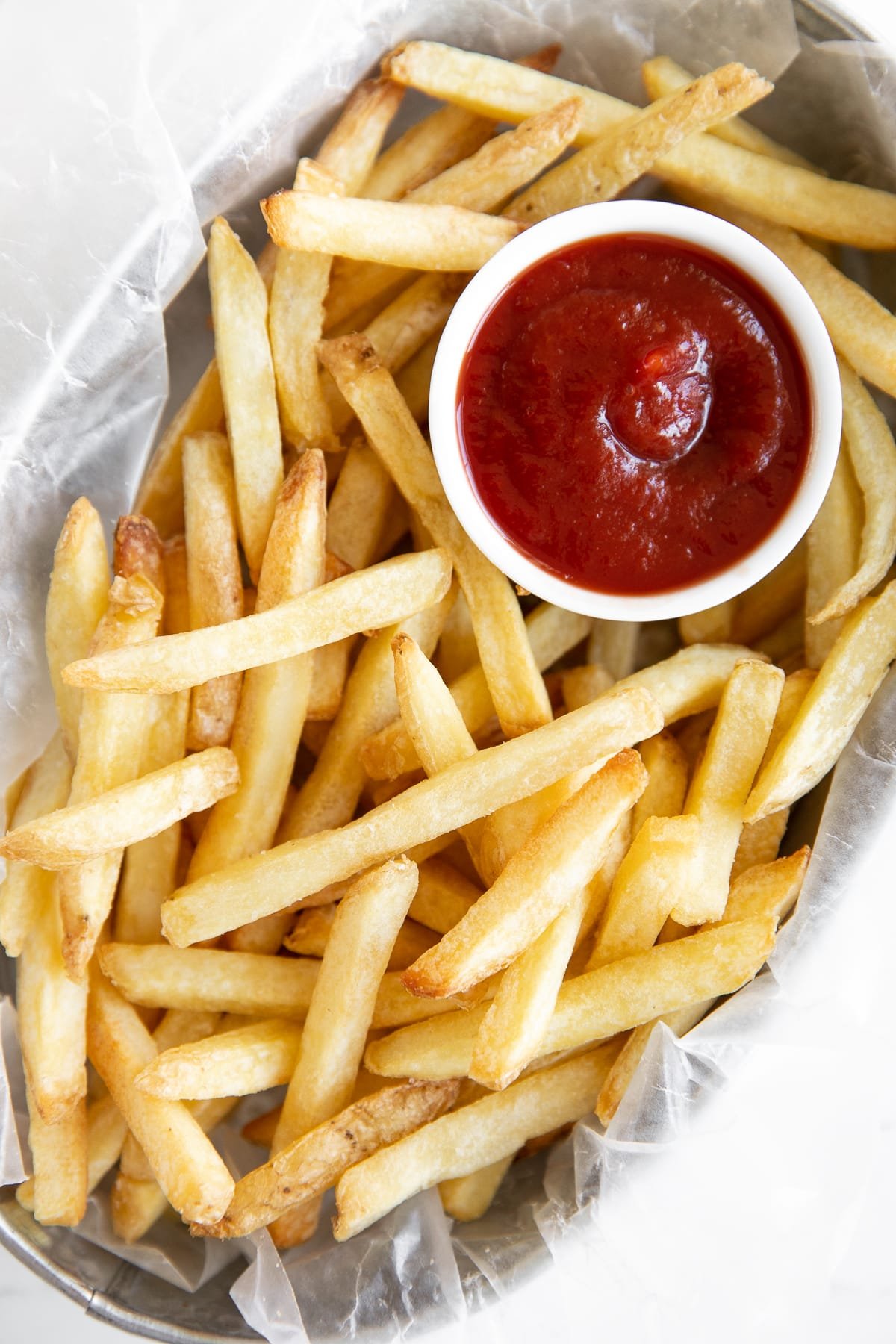 Metal serving basket filled with store-bought cooked frozen french fries and a small bowl of ketchup.
