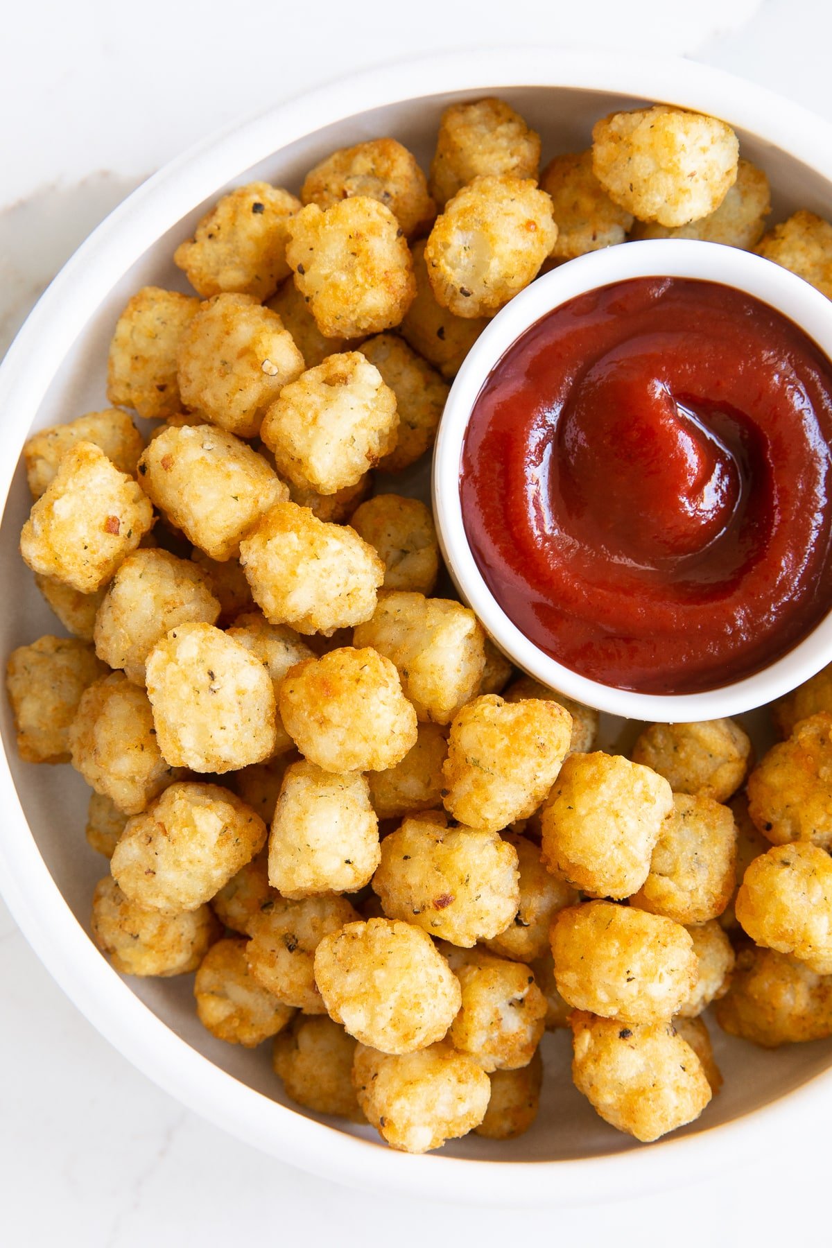 Round shallow plate filled with air fryer tater tots and a small bowl of ketchup.