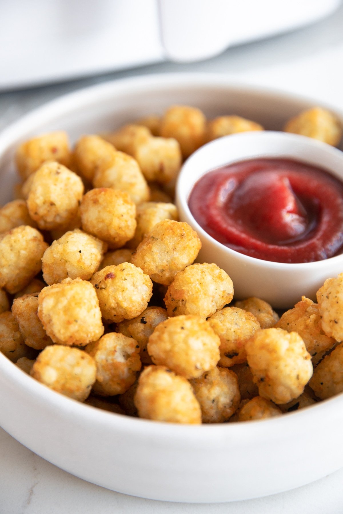 Golden air fryer tater tots on a large shallow plate with a small side of katchup.