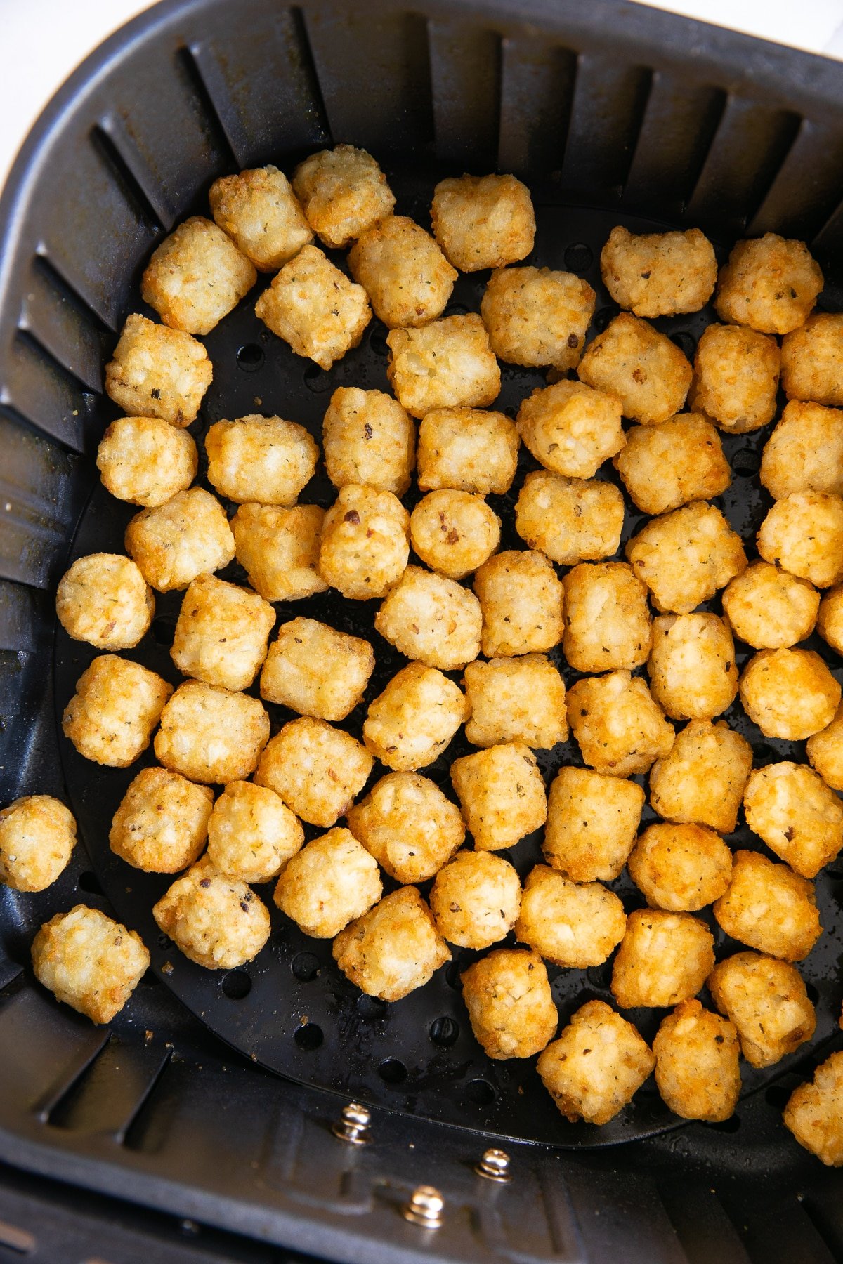 Air fryer basket filled with cooked golden crispy tater tots.