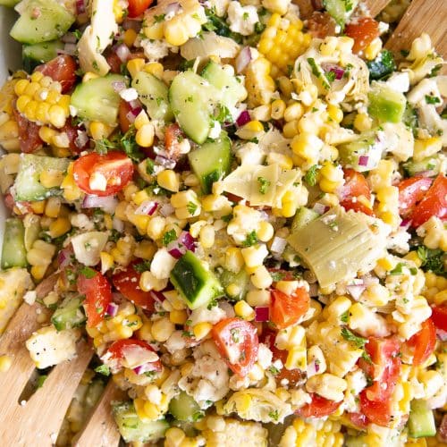 Corn salad tossed together in a large white platter with a blue trim.