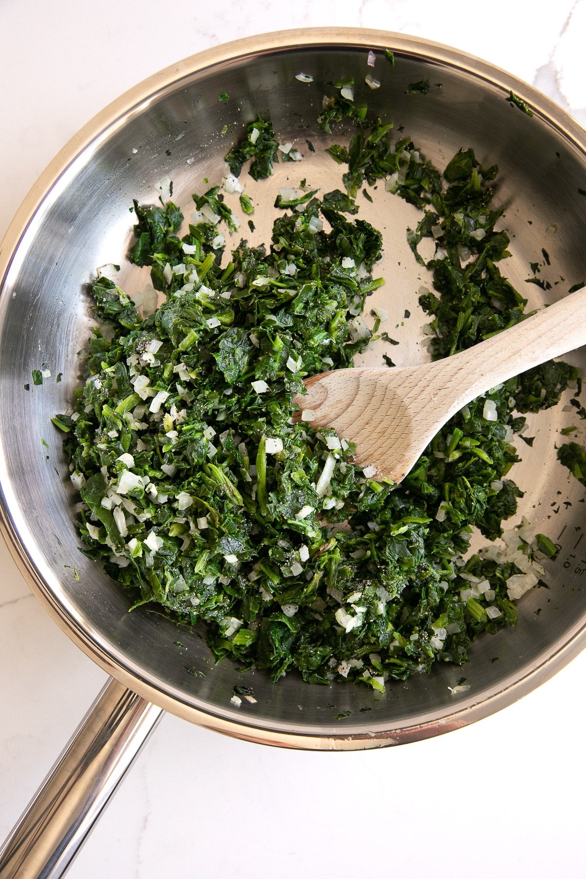 Skillet filled with sauteed chopped shallots and spinach.
