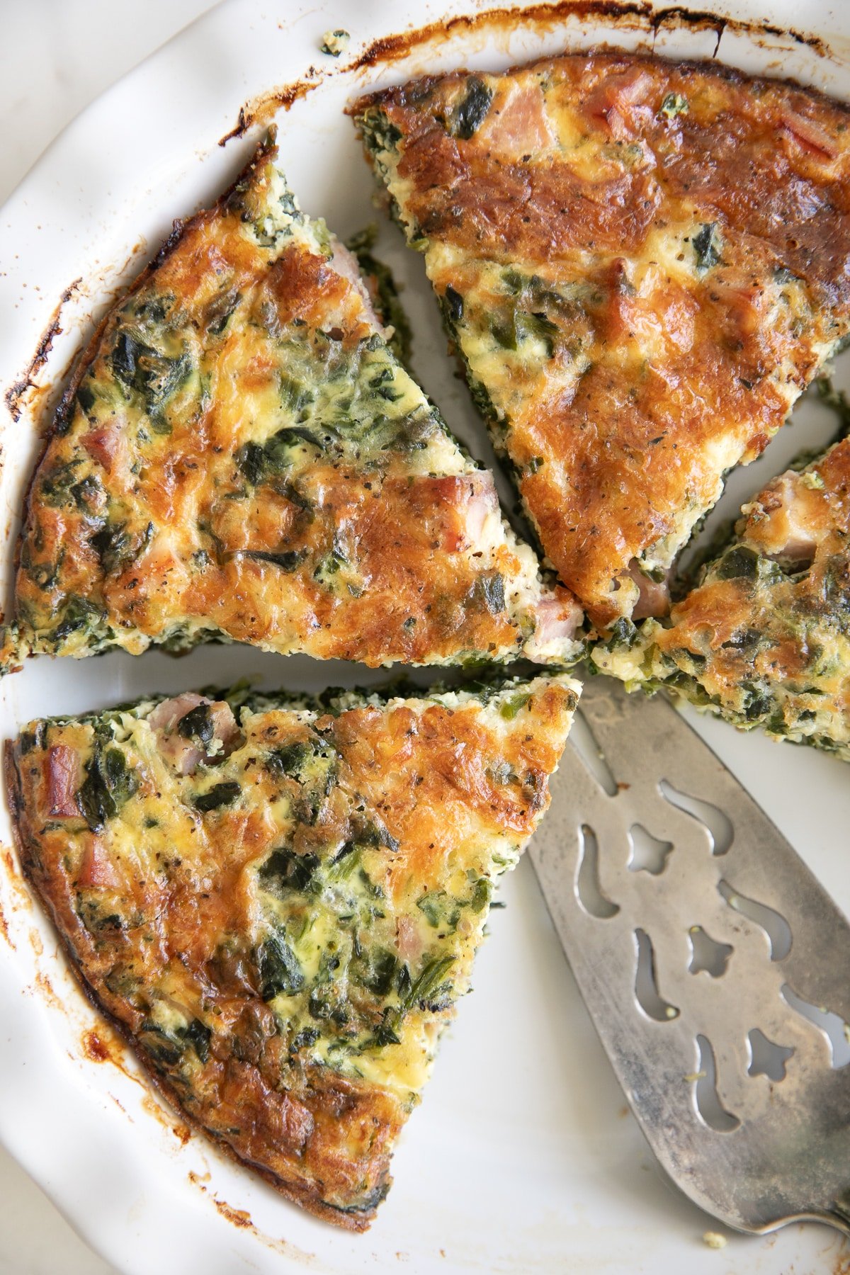 White pie dish filled with cooked crustless spinach quiche cut into slices.