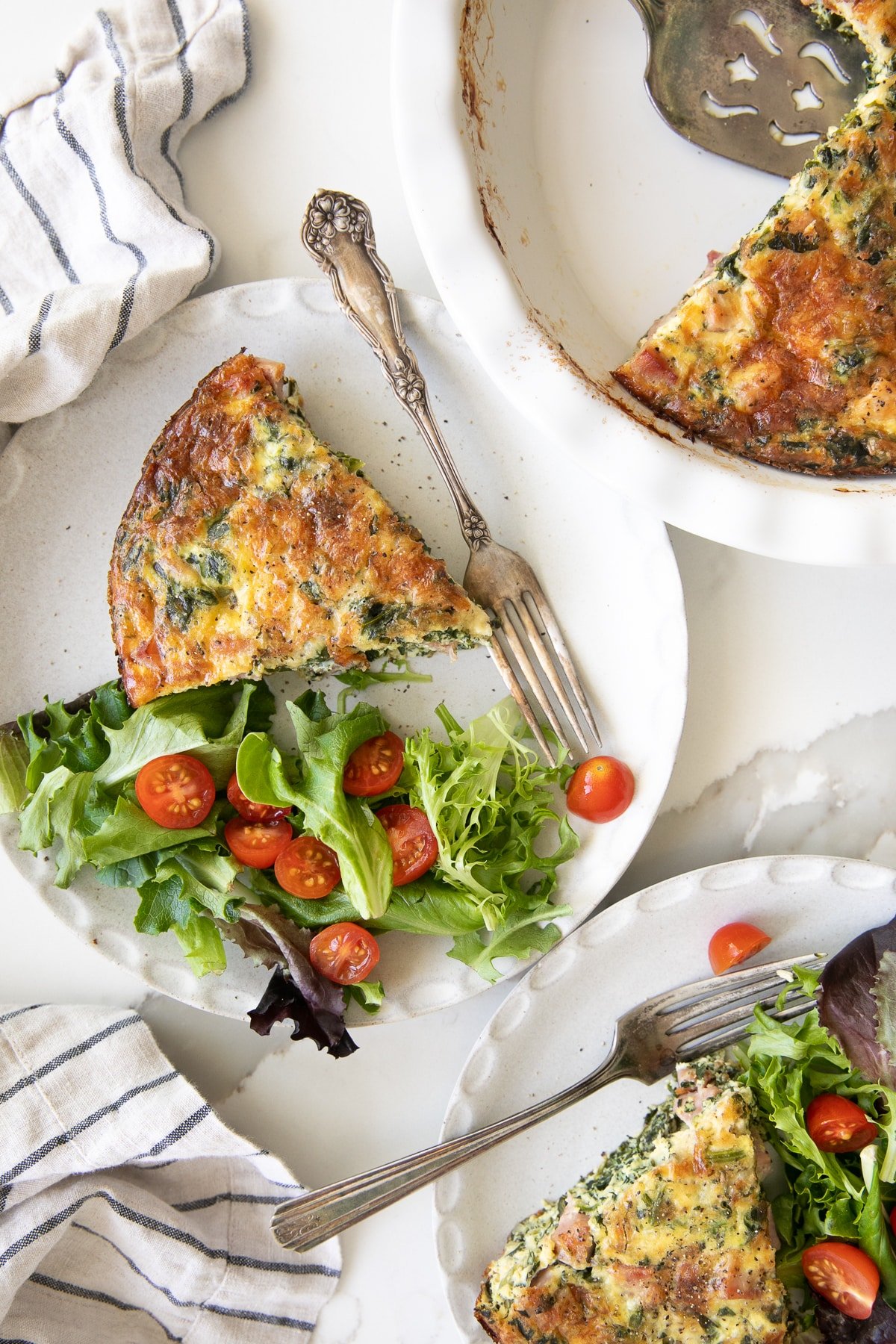 Two white serving plates with a slice of crustless quiche with broccoli and a side od spring salad with tomatoes.