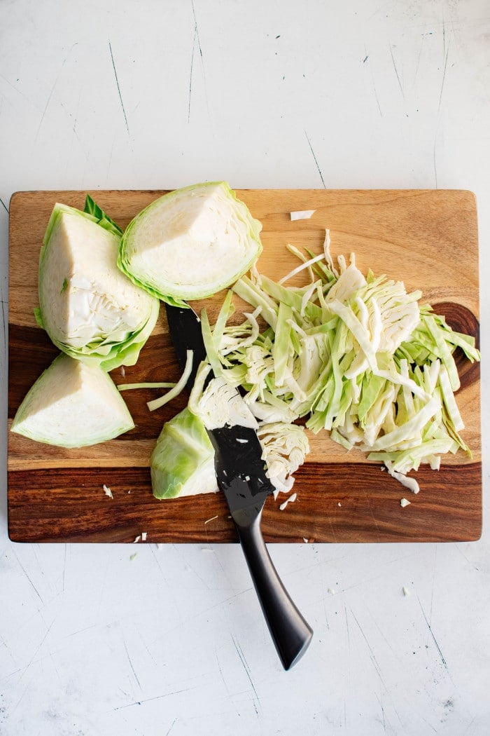 Slicing green cabbage into thin strips on a cutting board.