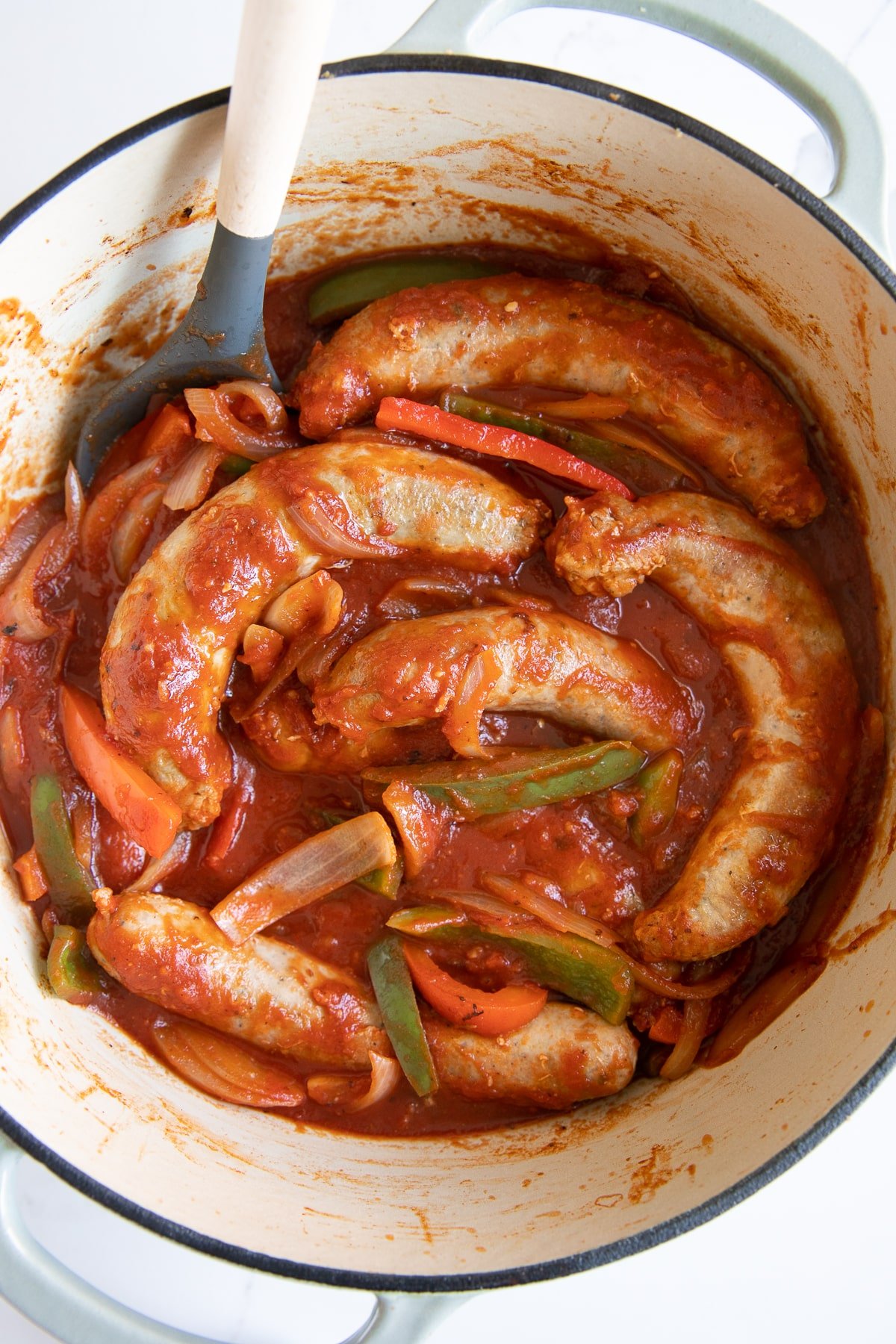 Large Dutch oven filled with sausage and pepper and onions simmering in tomato sauce.