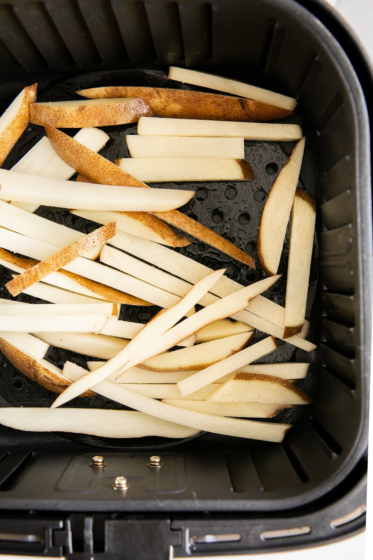 Uncooked potato sticks placed in a COSORI air fryer basket, ready to be cooked.
