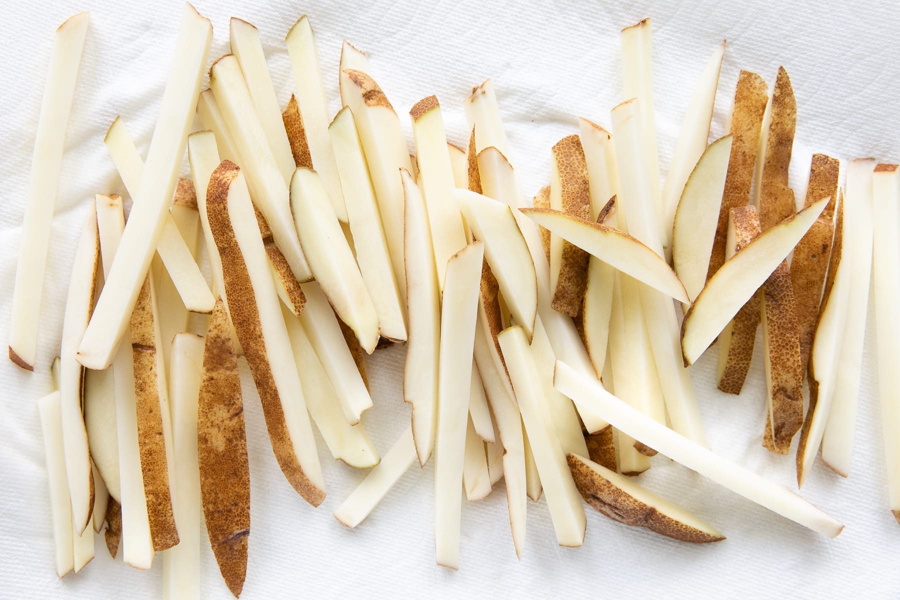 Raw russet potatoes sliced into uniform ¼-inch sticks, arranged on a white paper towel to dry before cooking.