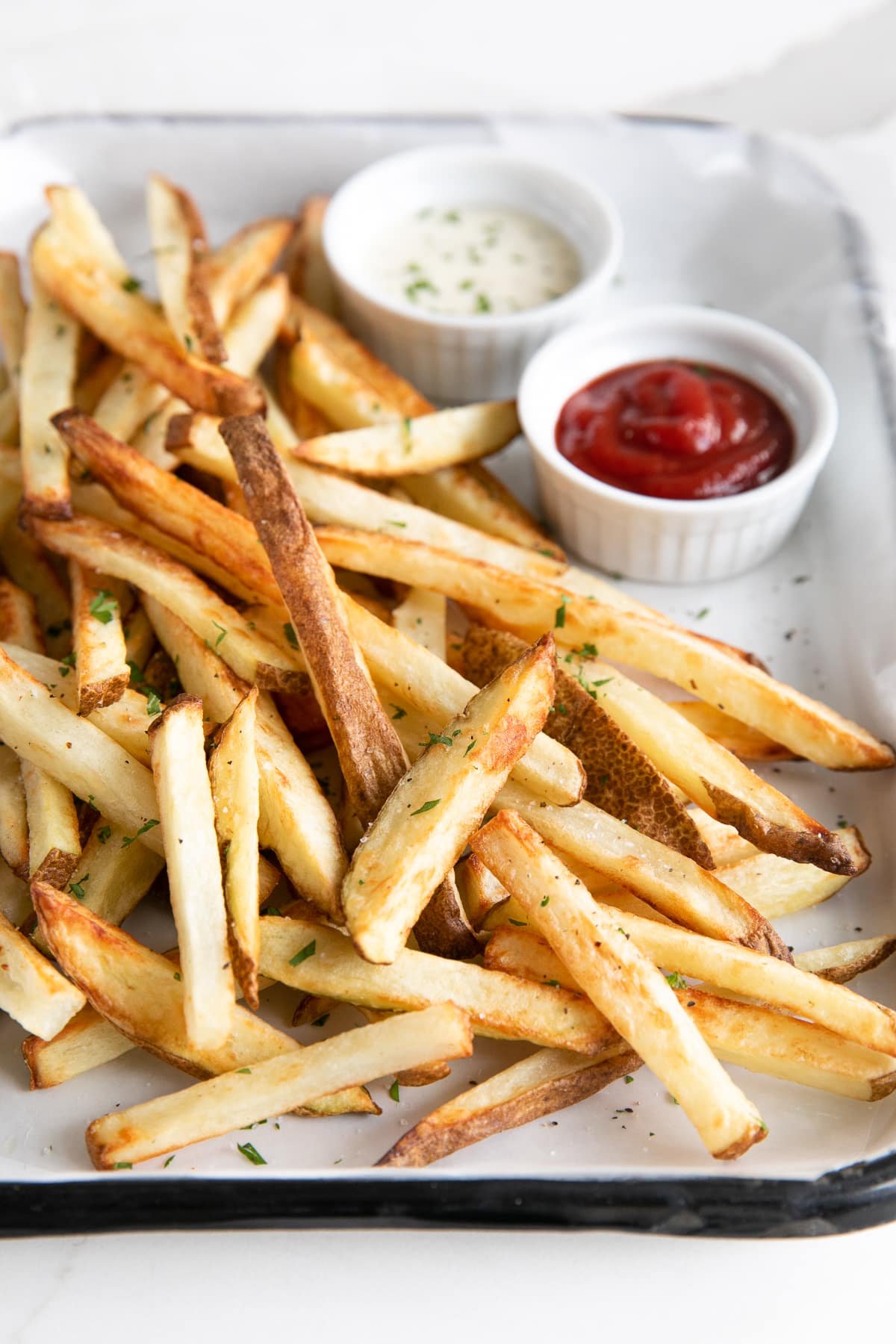 Crispy golden French fries served on a tray with small ramekins of ketchup and ranch dressing for dipping.