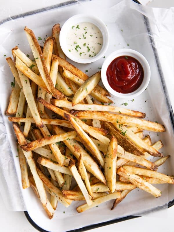 Overhead view of a tray of golden brown air fryer French fries with ketchup and ranch on the side.